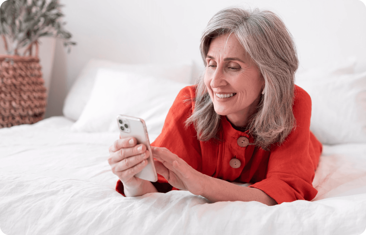 Imagem de uma mulher deitada na cama usando o celular e sorrindo